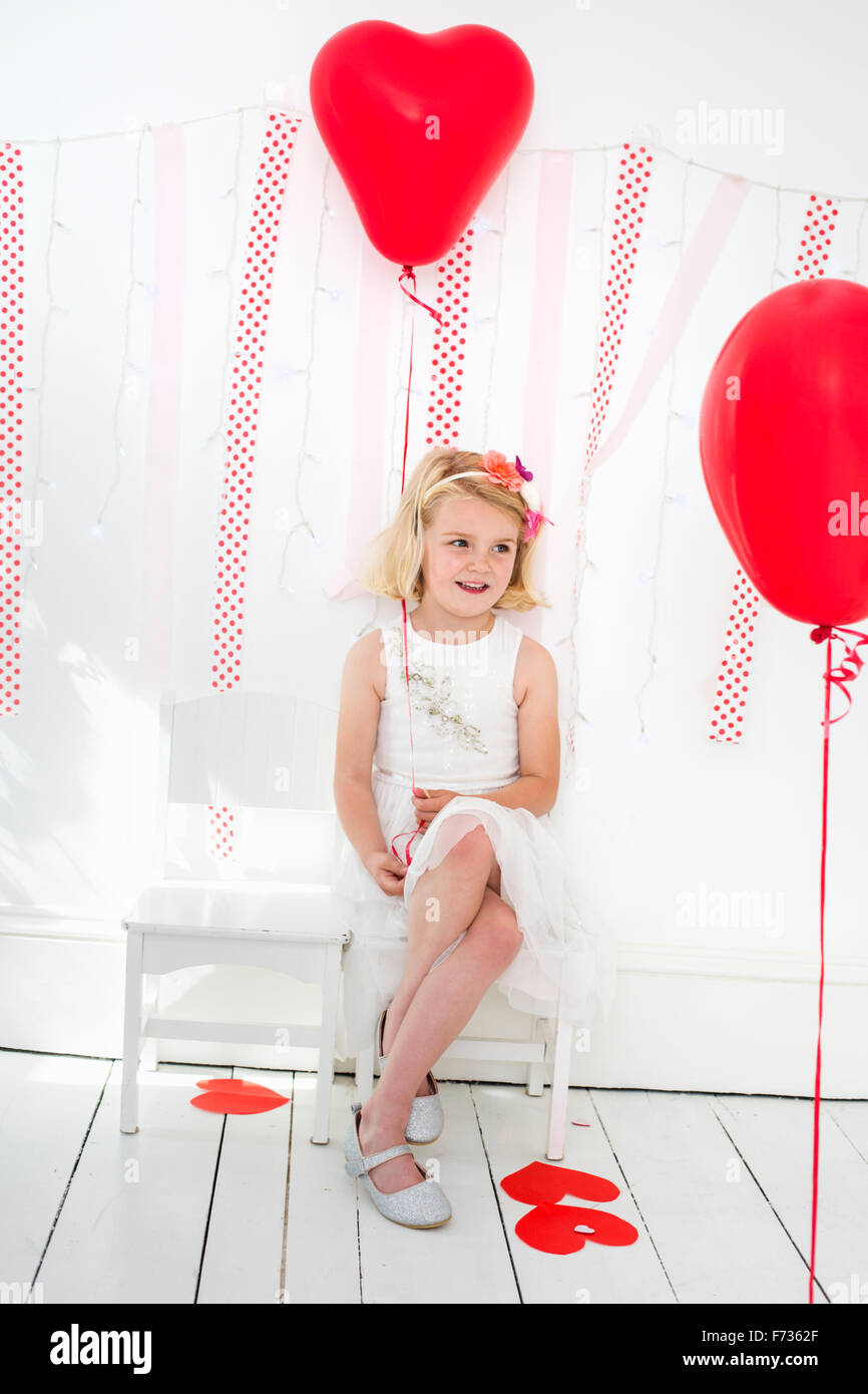 Young girl posing for a picture in a photographers studio, surrounded by red balloons. Stock Photo