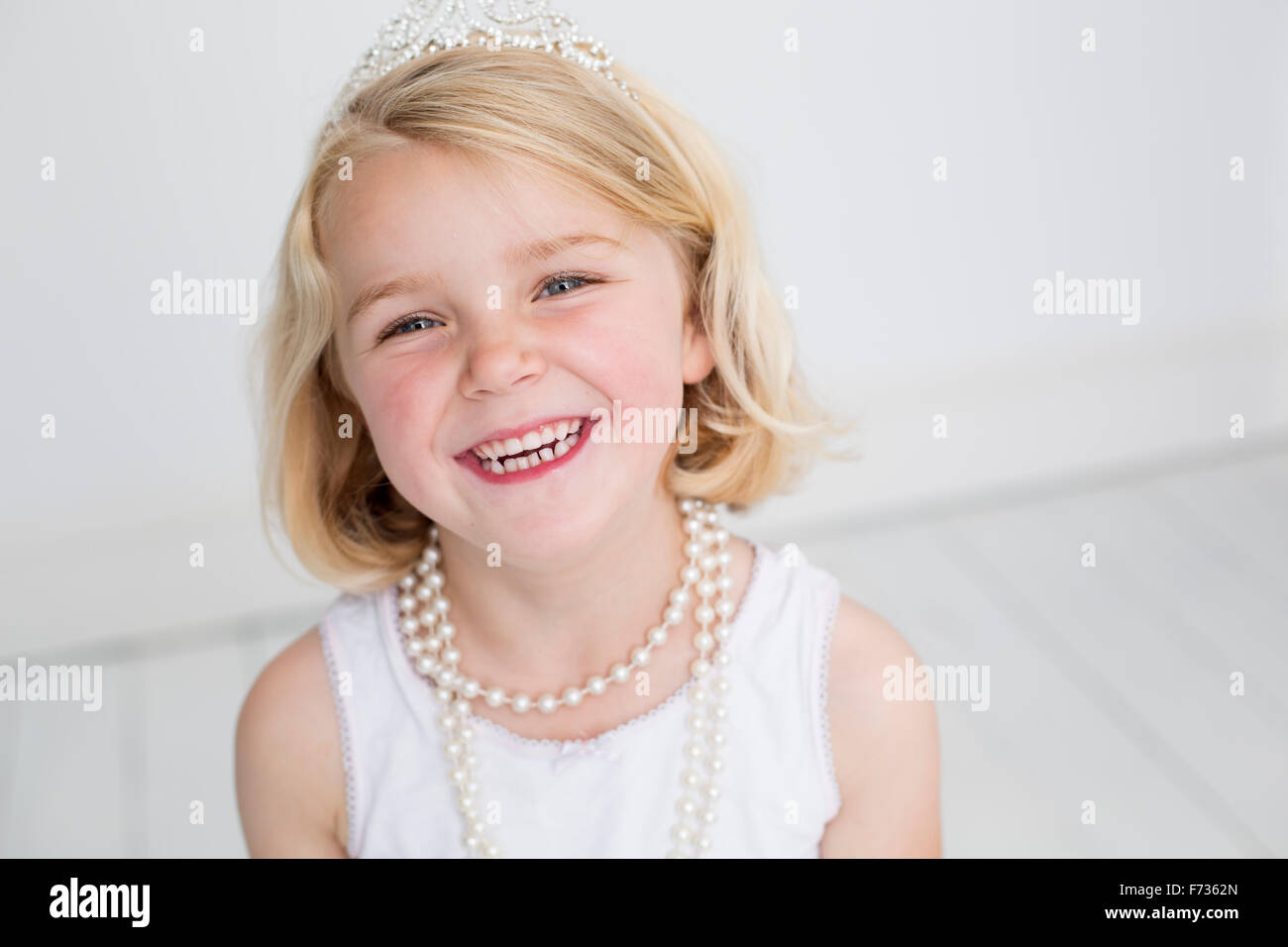 Young girl wearing a tiara and a pearl necklace, posing for a picture in a photographers studio. Stock Photo
