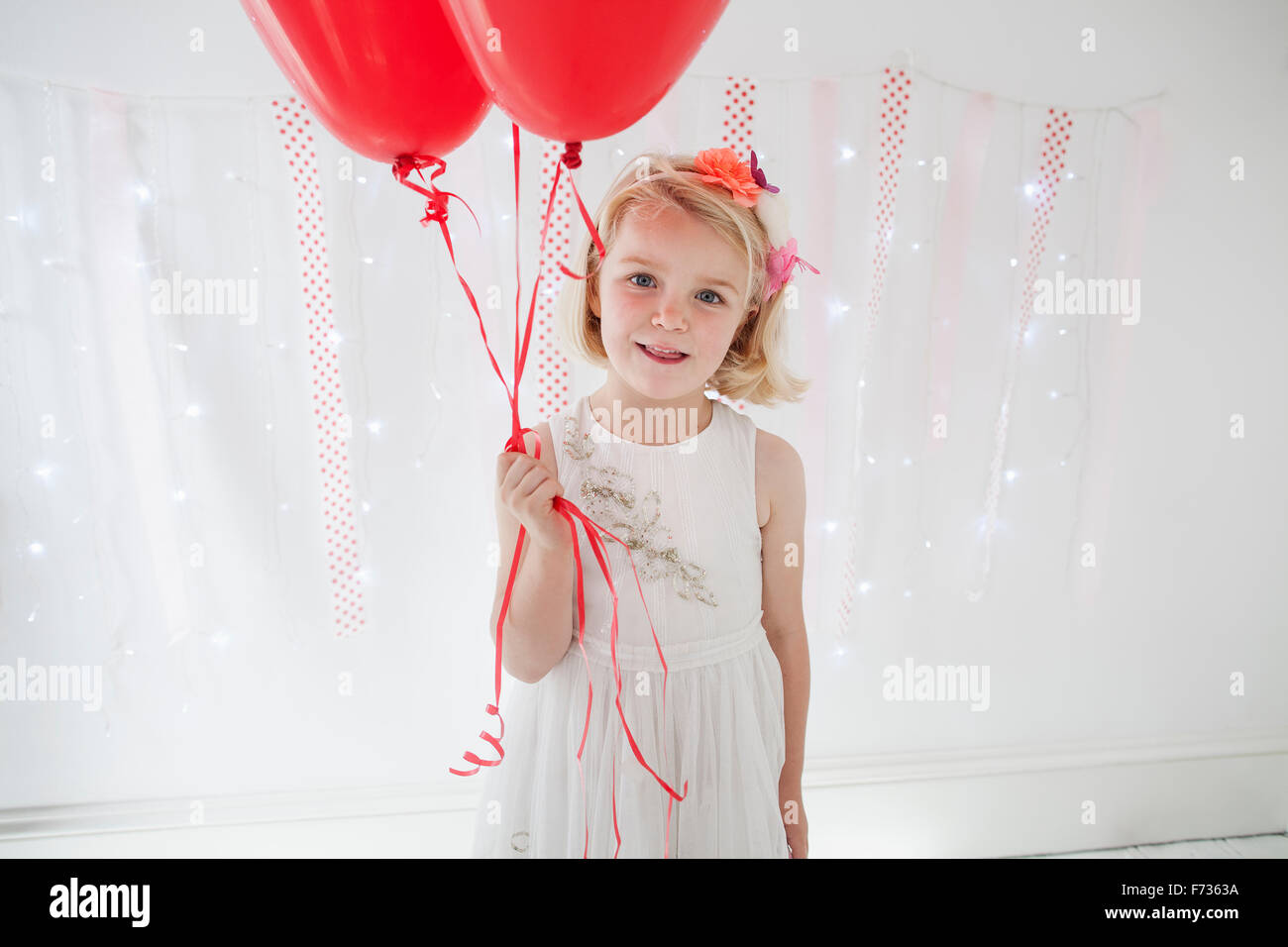 Young girl posing for a picture in a photographers studio, holding red balloons. Stock Photo