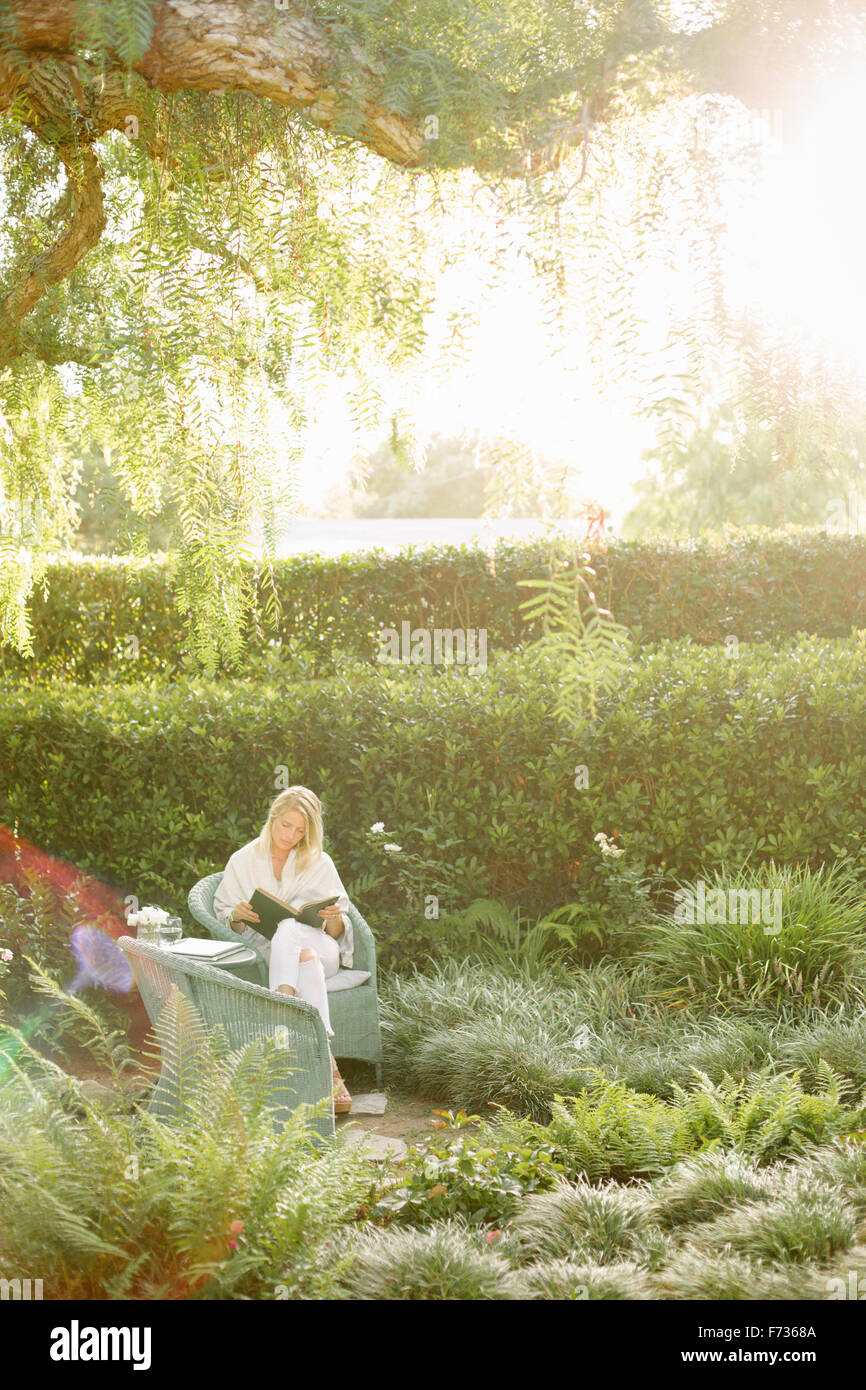 Blond woman sitting in a wicker chair in a garden, reading Stock Photo ...