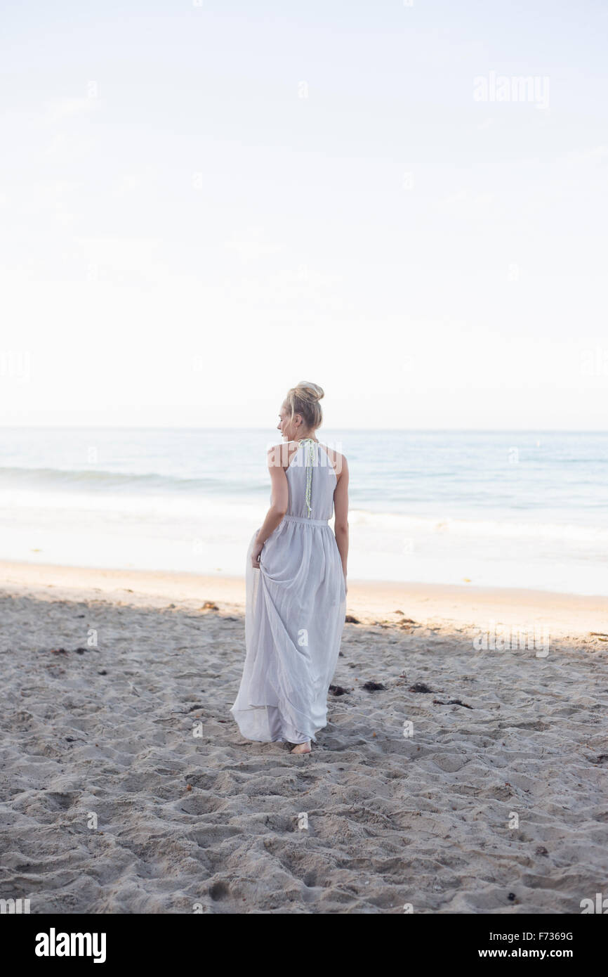 Blond woman wearing a long dress standing on a sandy beach. Stock Photo