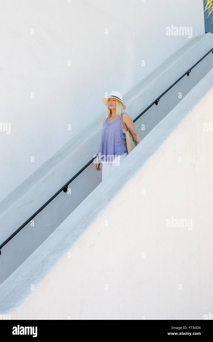 Blond woman wearing a hat walking down a staircase. Stock Photo