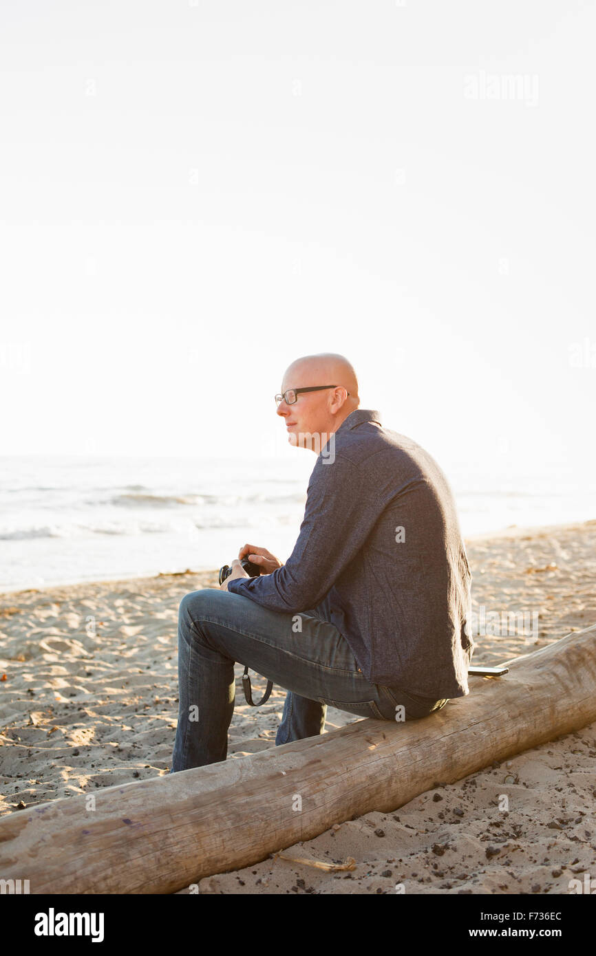 Bald man sitting on a log on a sandy beach. Stock Photo