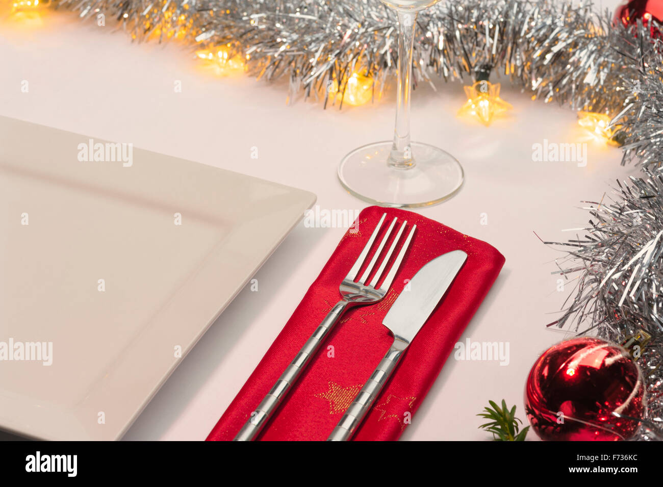 Table laid for Christmas dinner, decorated with baubles and tinsel and fairy lights. Knife fork and red napkin. Stock Photo