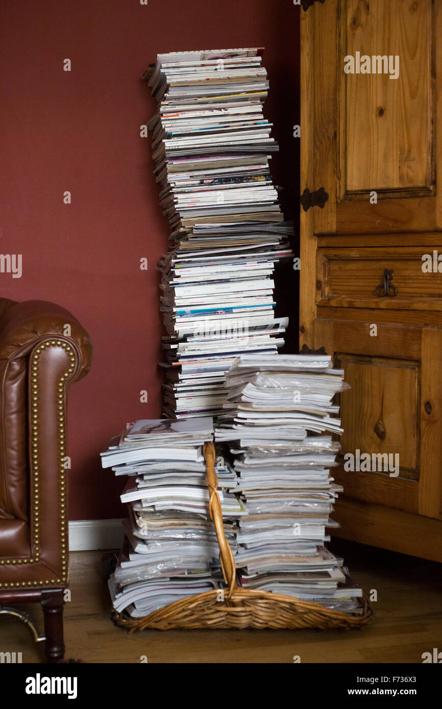 Tall stack of magazines in a basket leaning against a wall. Stock Photo