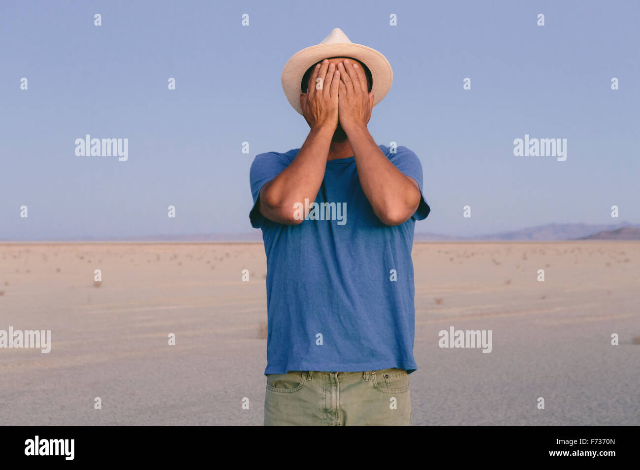 A man in an open desert landscape covering his face with his hands. Stock Photo