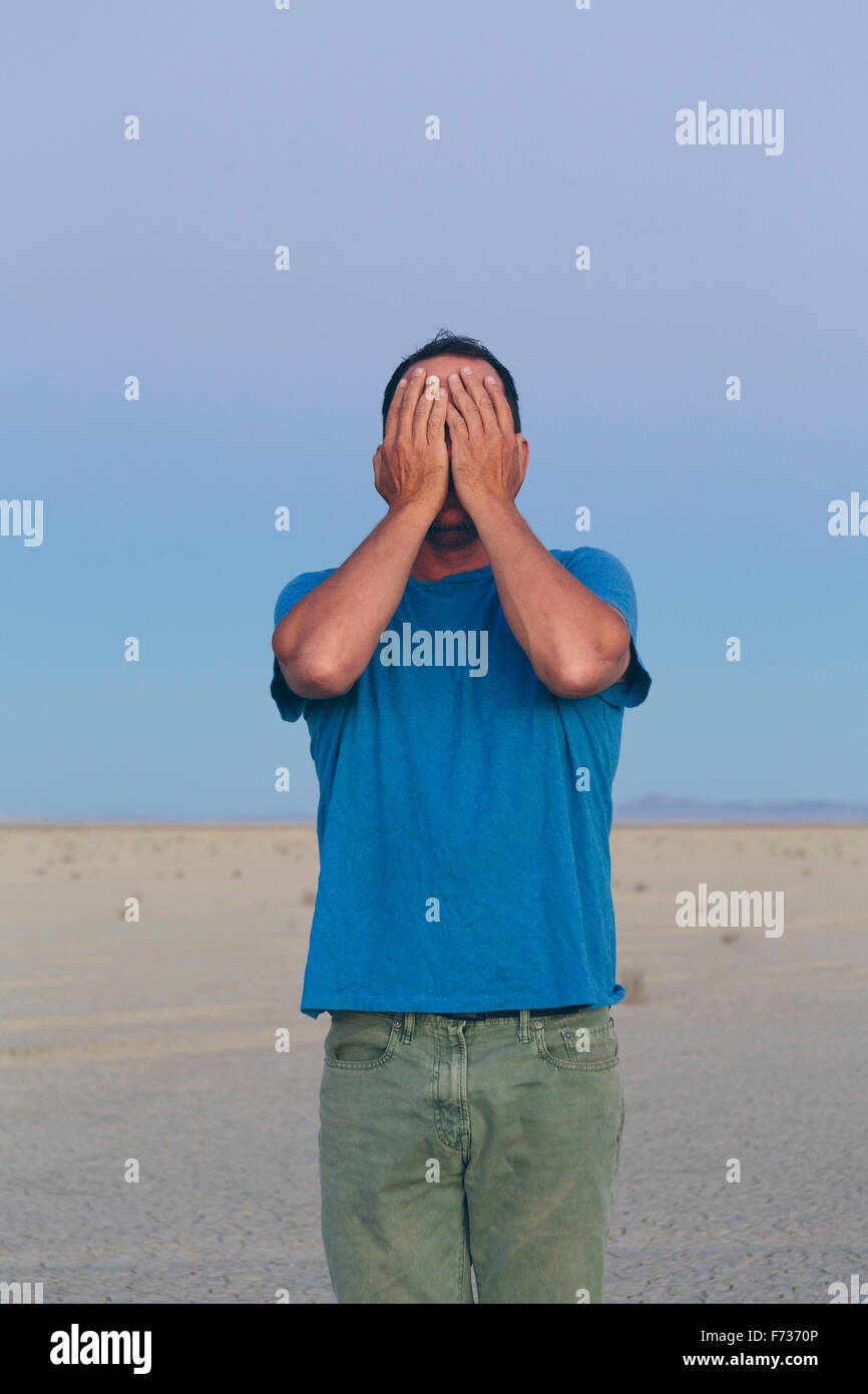 A man in open desert landscape covering his face with his hands. Stock Photo