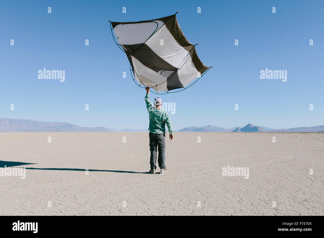 Man holding a capsule pod camping tent above his head in the open space of the desert. Stock Photo