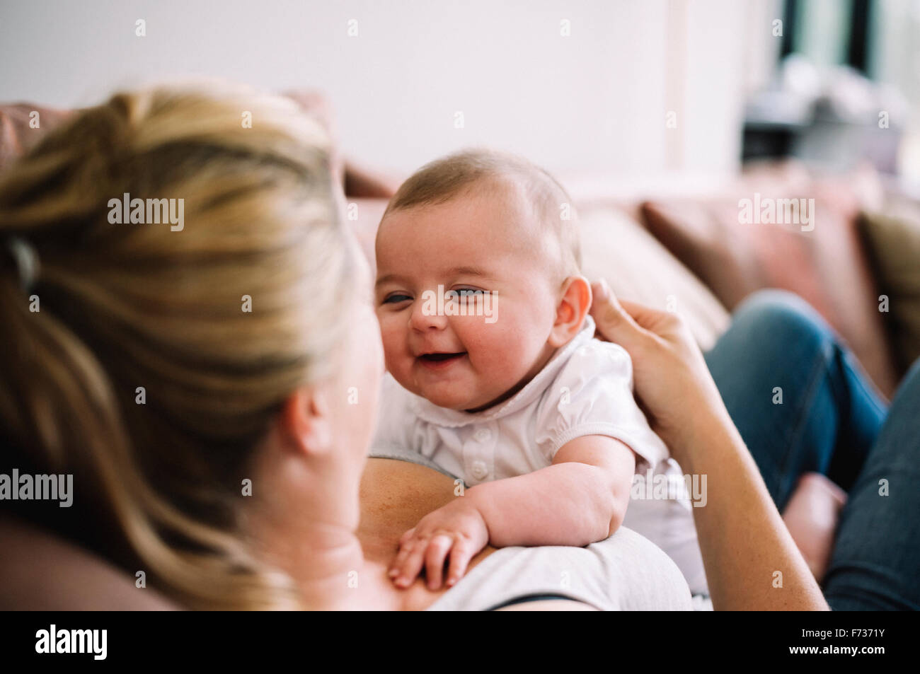 A woman lying on a sofa playing with a baby girl. Stock Photo