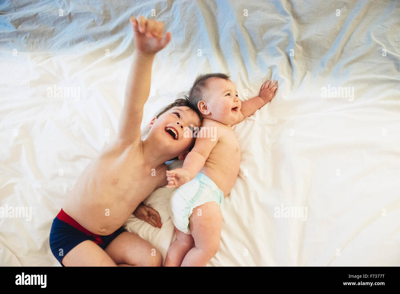 Two children, a brother and baby sister lying down playing together. Stock Photo
