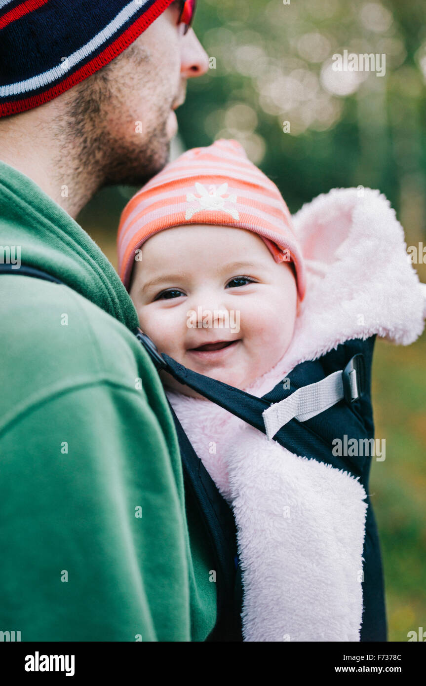 A baby in a sling being carried by her father, outdoors in winter Stock