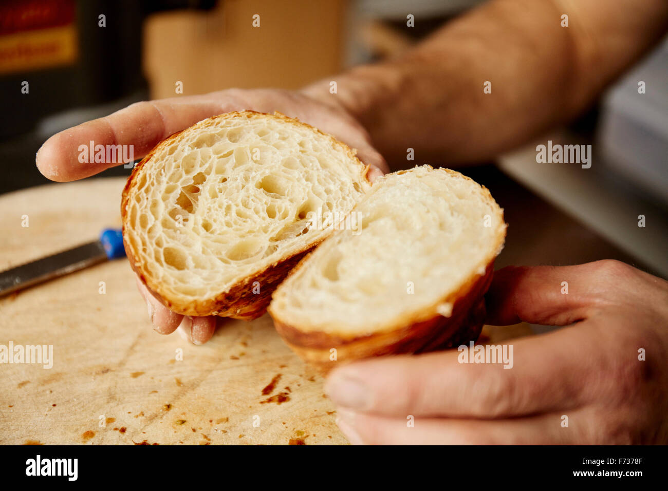 A man holding a croissant cut in half, to show the light layered