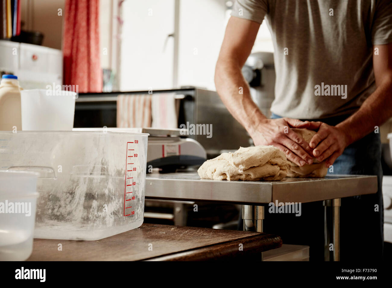 A man, a baker working in a commercial kitchen kneading a large piece of dough. Stock Photo