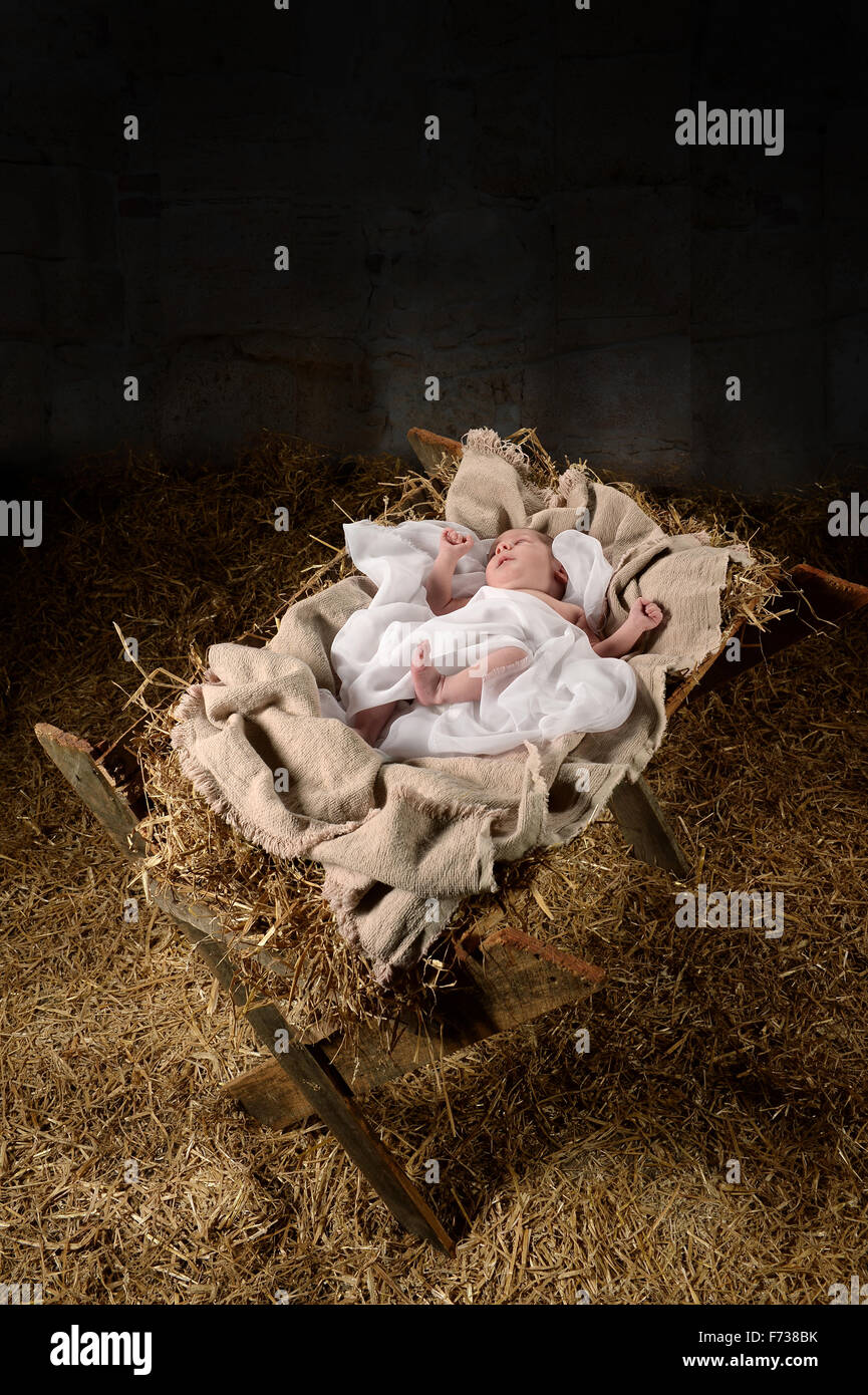Baby Jesus on a manger inside old dark stable Stock Photo