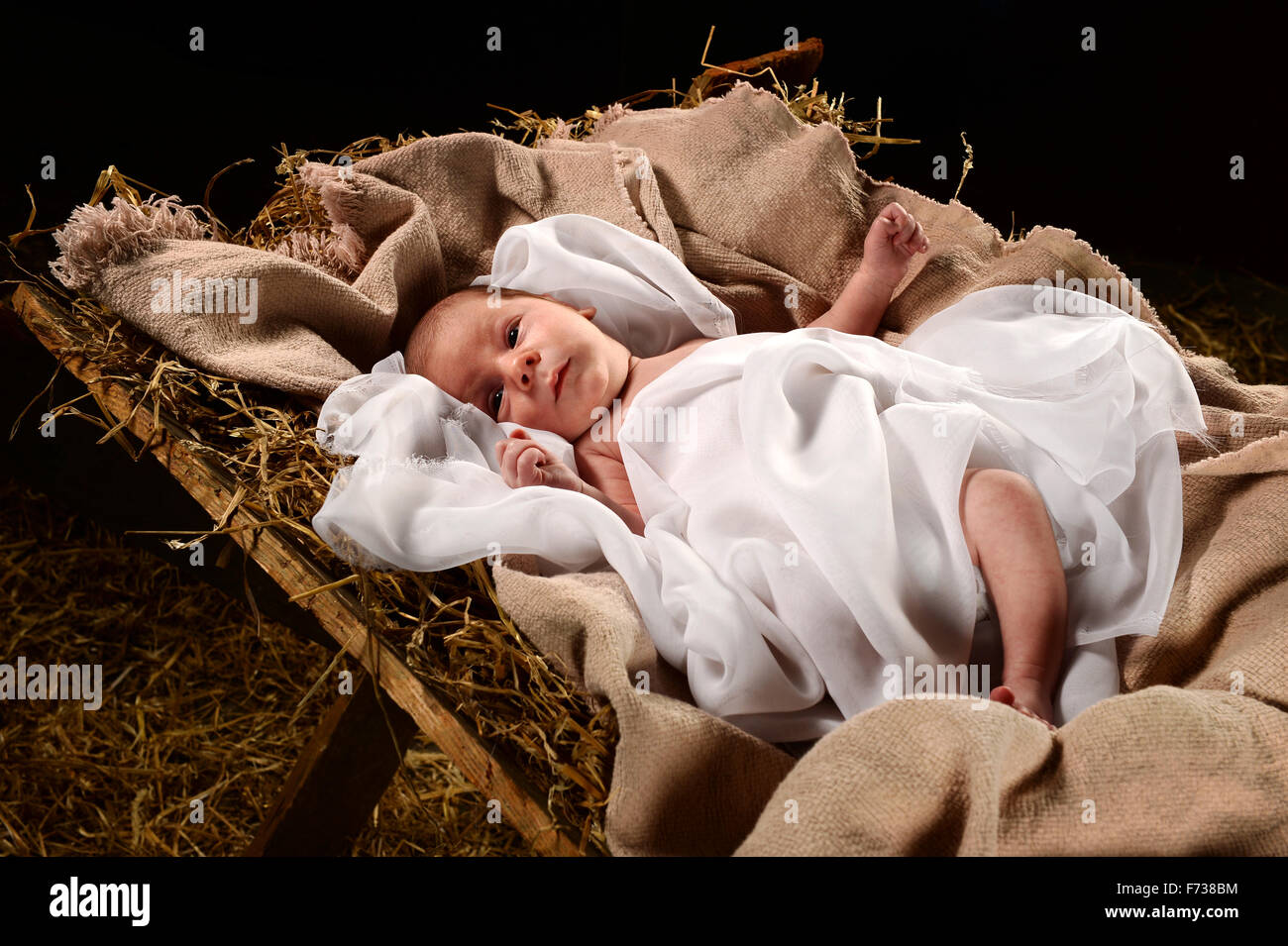 Baby Jesus when born on a manger wrapped in swaddling clothes over dark background Stock Photo