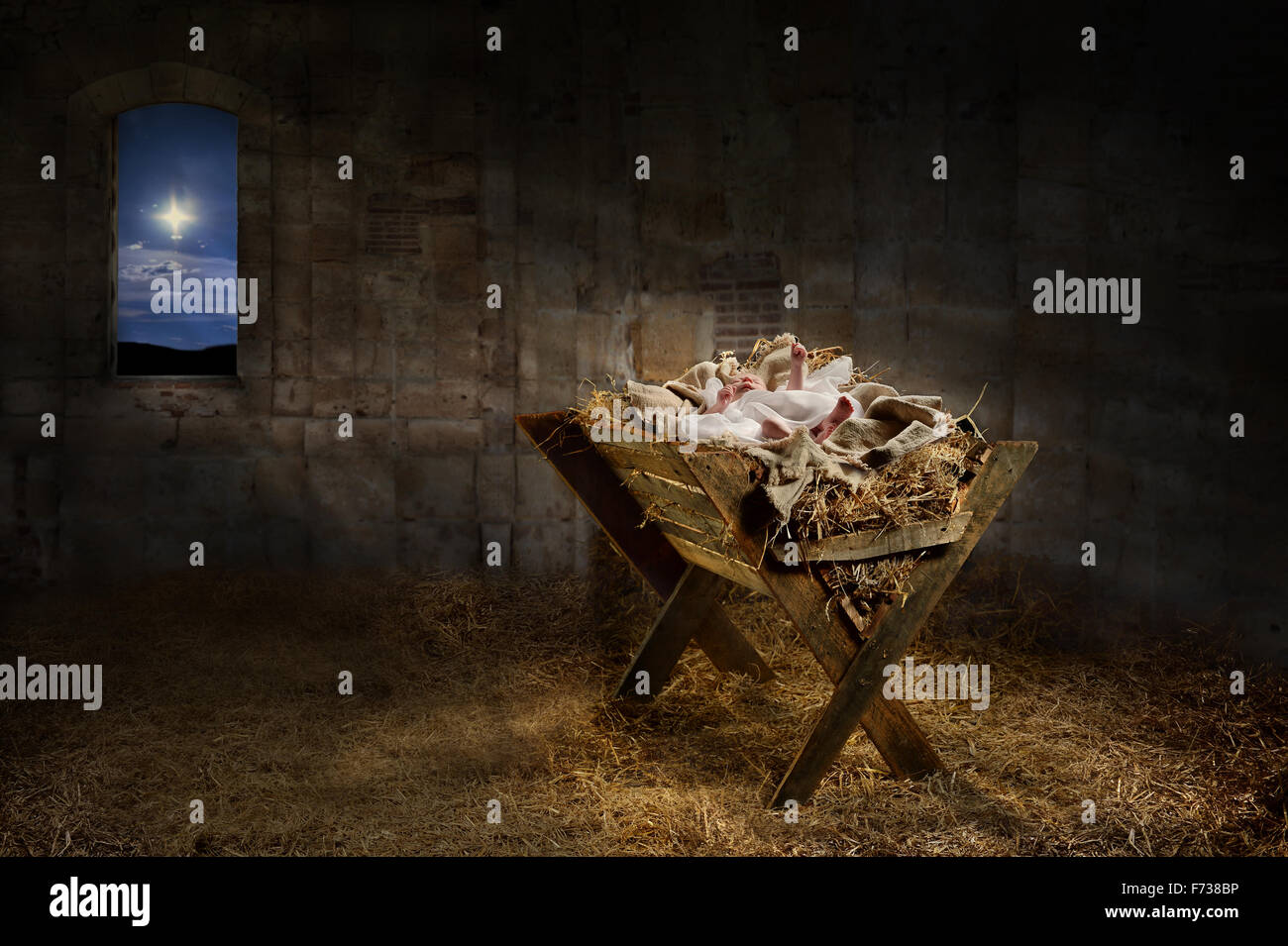 Jesus resting on a manger while light from the star filters into the room Stock Photo