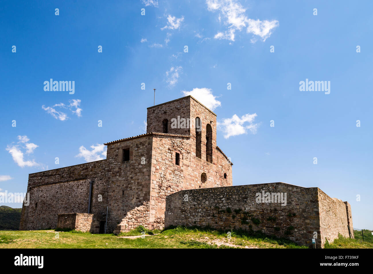 An old Spanish church sits on top of a grassy hill with a blue sky overhead. Stock Photo