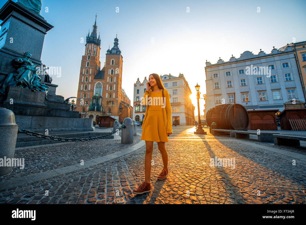 Young and beautiful woman in yellow dress walking and talking with mobile phone in the old city center of Krakow on the morning  Stock Photo