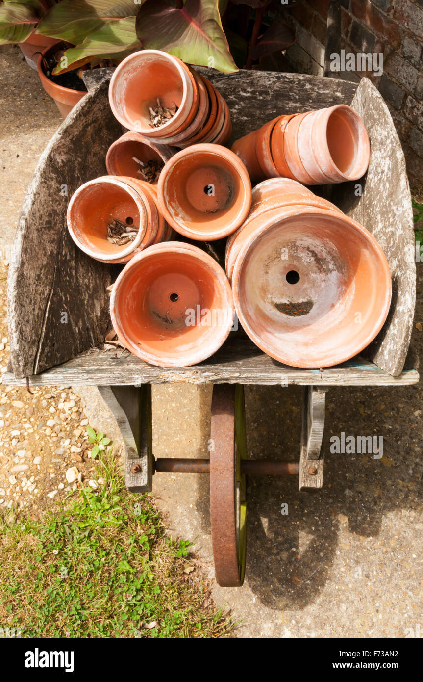 An old wooden wheelbarrow full of earthenware flower pots. Stock Photo