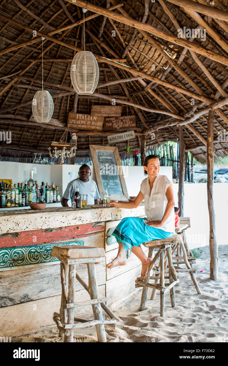 MANDA ISLAND, LAMU, KENYA, AFRICA. A young woman sits at a thatch-roof ...