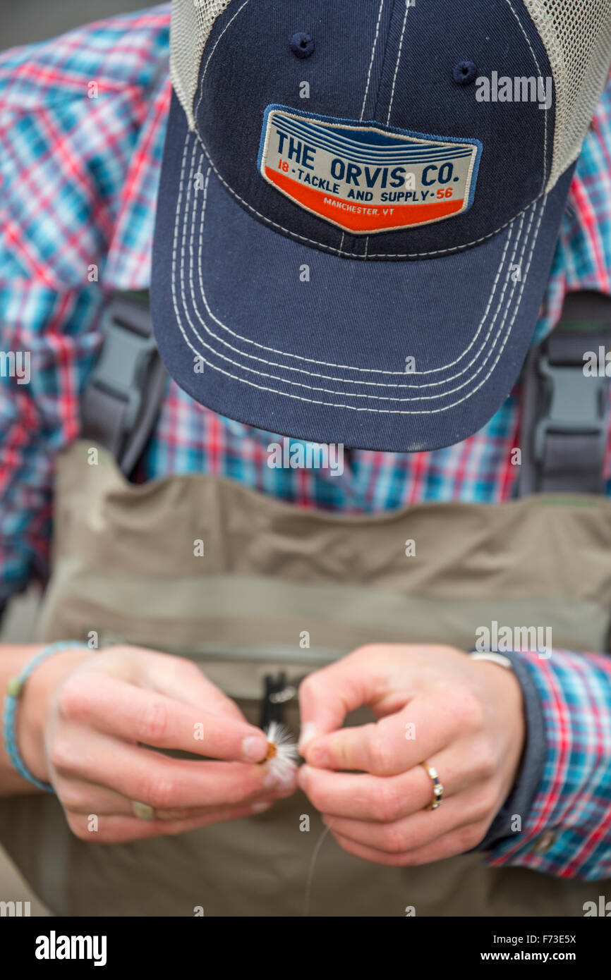 An angler ties on a new fly while wearing Orvis gear. Stock Photo