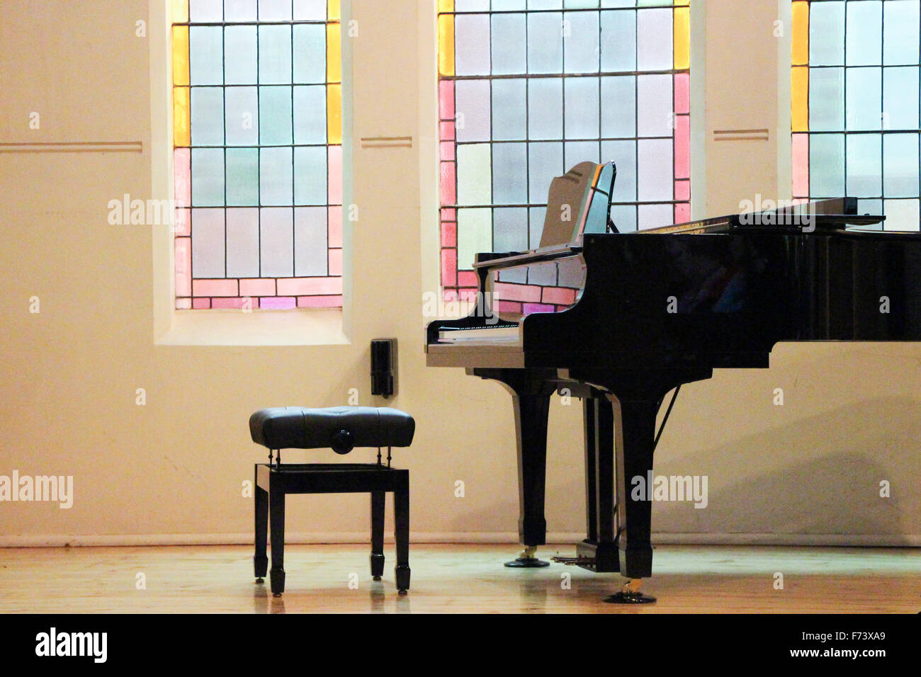 Beautiful stained glass windows in a church reflecting onto a shiny black grand piano. Stock Photo