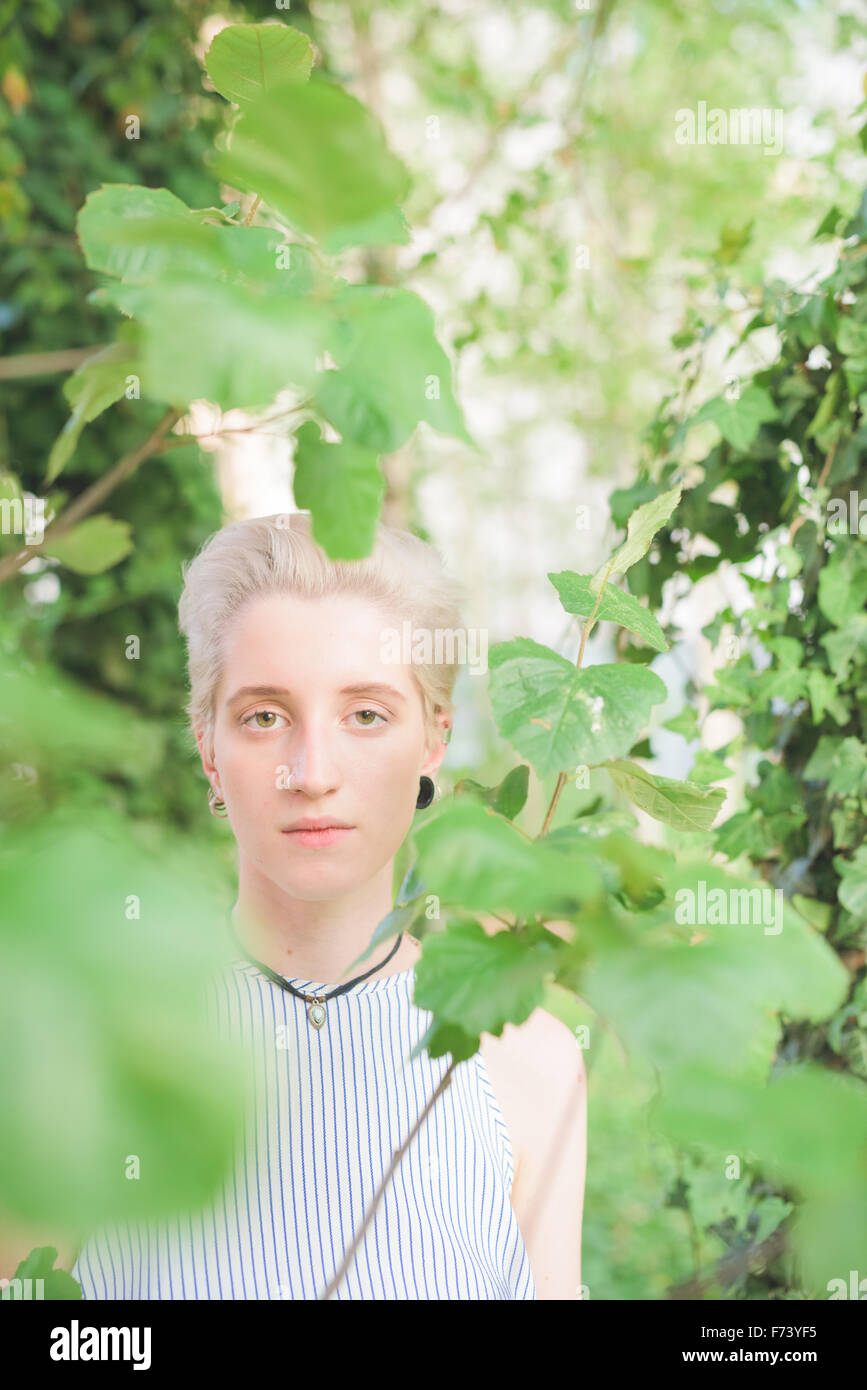 Half length portrait of young handsome caucasian blonde italian designer view behind some leaves - creative, nature concept Stock Photo