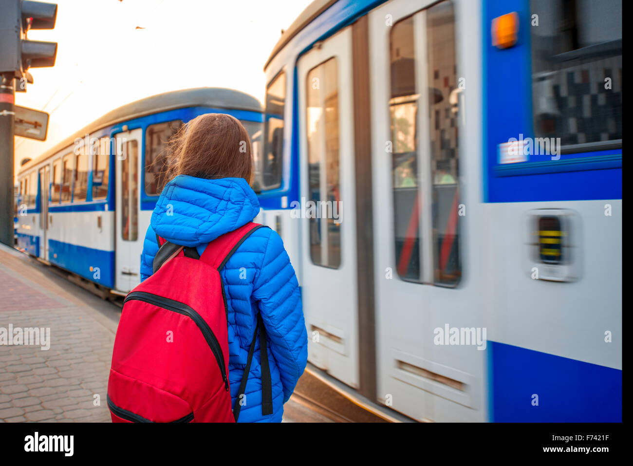 Young female tourist in blue jacket with backpack on the station with blue tram on backround. Motion effect Stock Photo