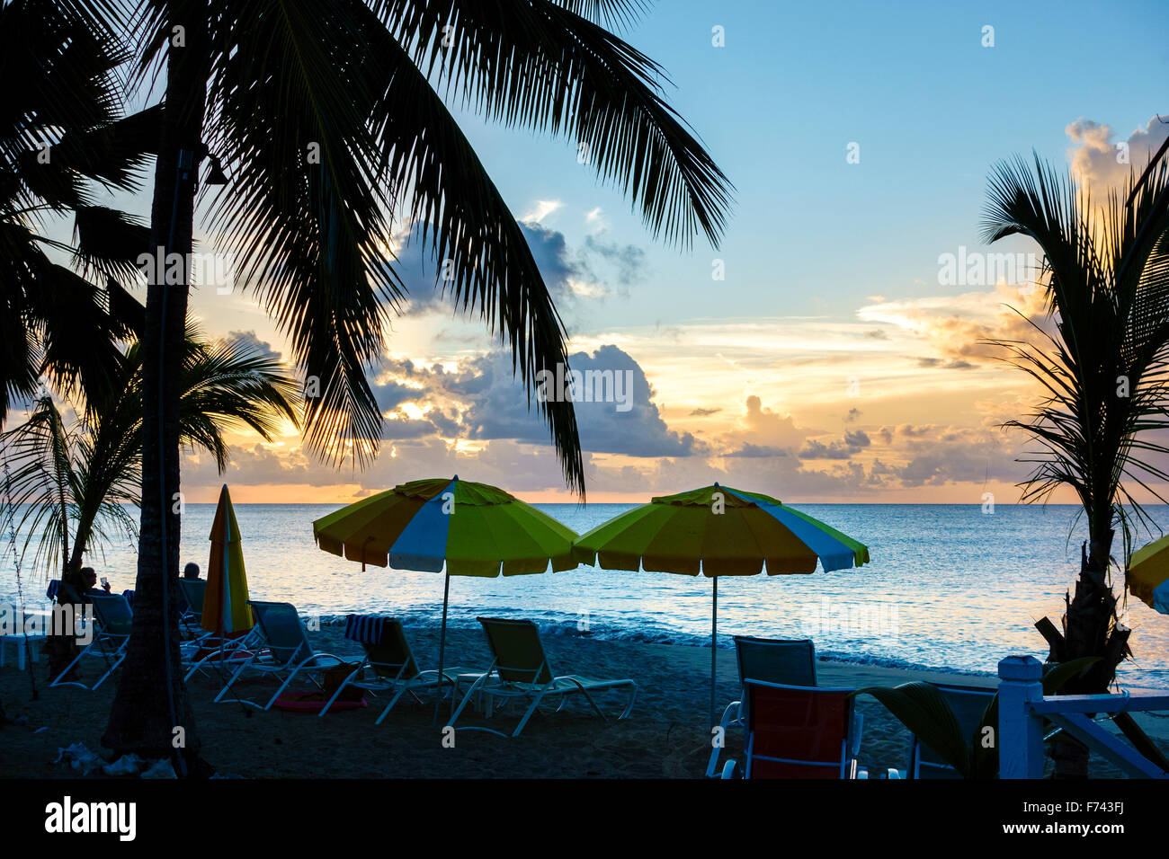 The beach at a resort at sunset, palm trees, chairs and beach umbrellas. St. Croix, U.S. Virgin Islands. USVI, U.S.V.I. Cottages by the Sea resort. Stock Photo