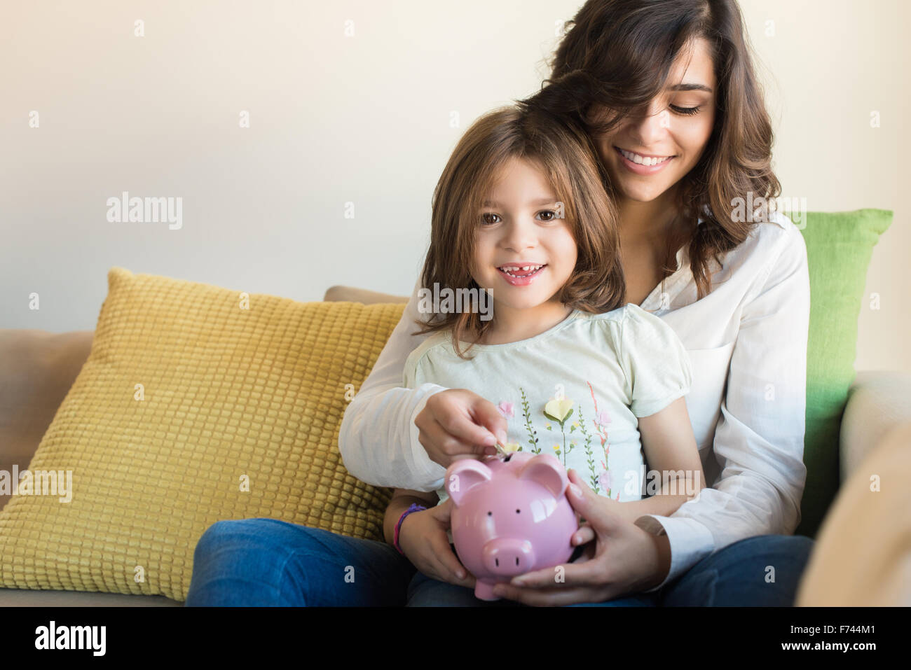 Mother and daughter putting coins into piggy bank Stock Photo - Alamy