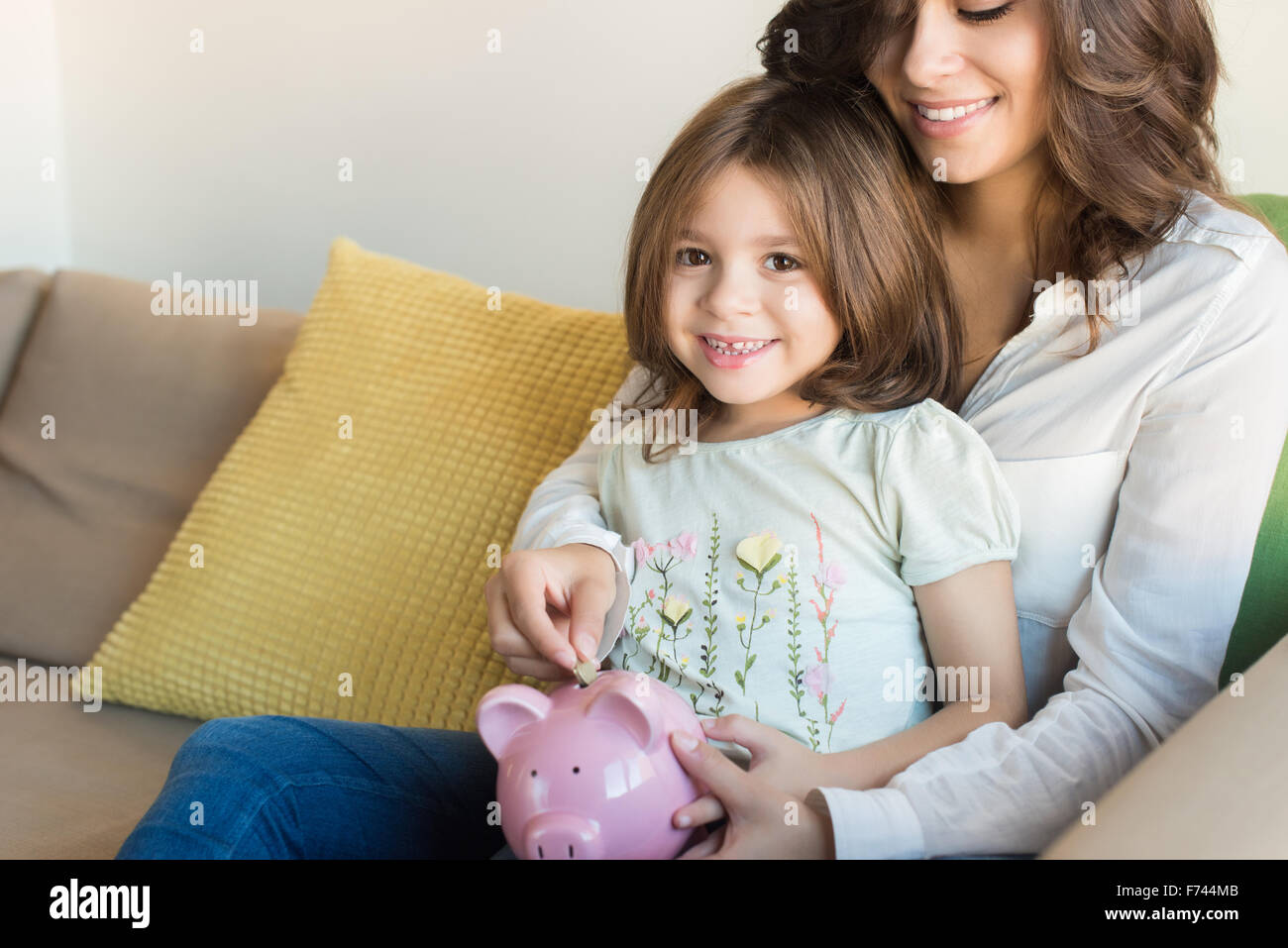 Mother and daughter putting coins into piggy bank Stock Photo - Alamy