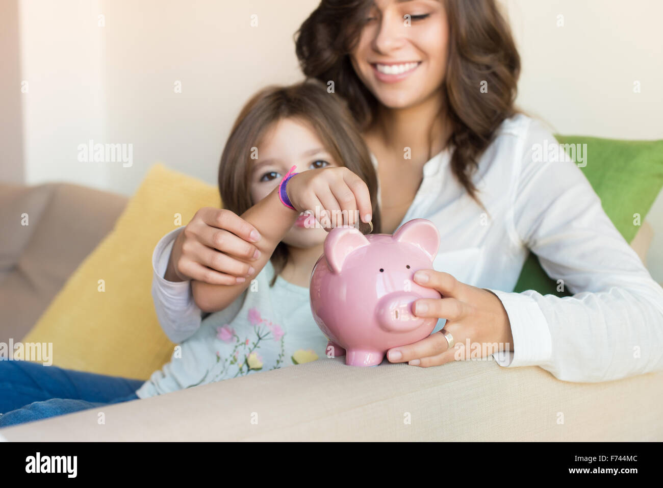 Mother and daughter putting coins into piggy bank Stock Photo - Alamy