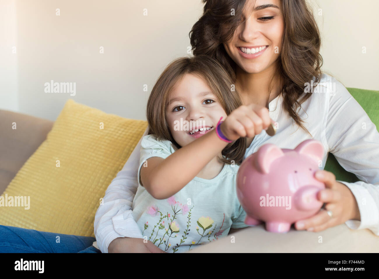 Mother and daughter putting coins into piggy bank Stock Photo - Alamy