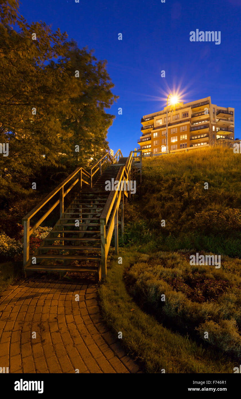 A wooden stairway leading to Lakeshore Road lit by street lights at dusk. Shipyard Park, Oakville, Ontario, Canada. Stock Photo