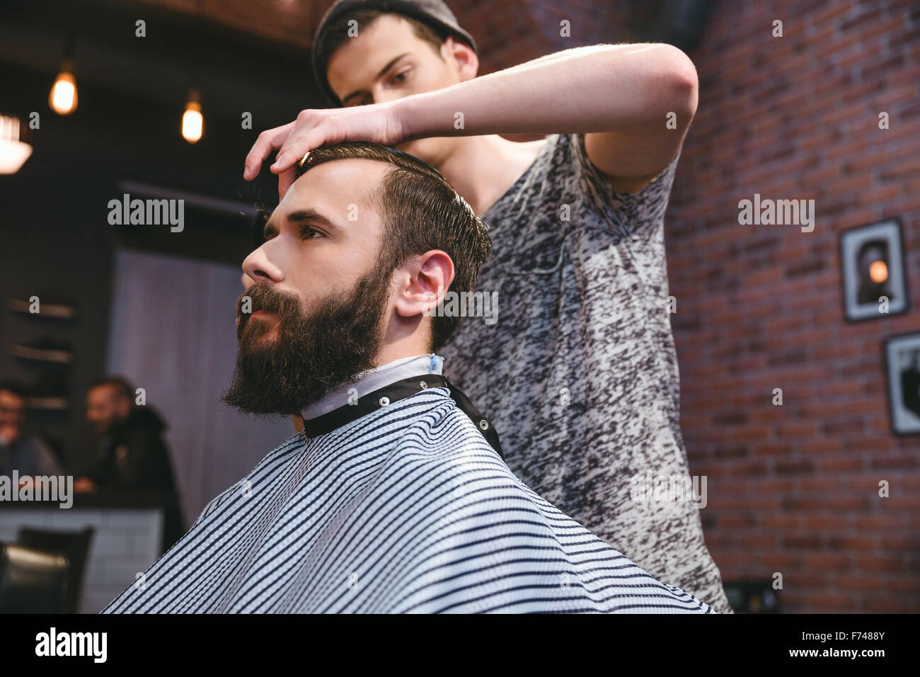 Young handsome barber cutting hair of young attractive bearded hipster in barbershop Stock Photo