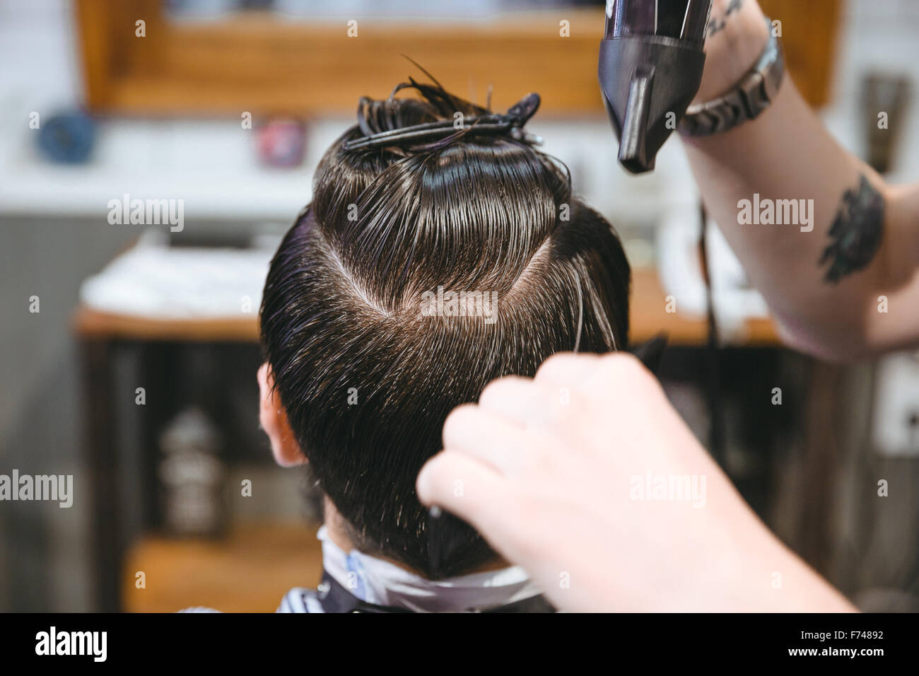 Closeup of hands of hairstylist drying hair of male client using hairdryer and comb in barbershop Stock Photo