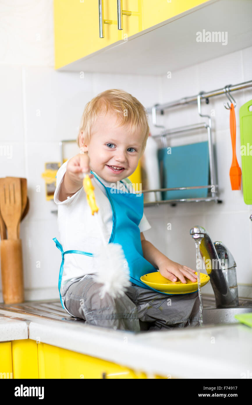 Happy toddler boy washing the dishes in the kitchen Stock Photo
