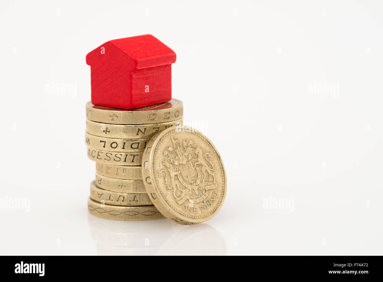 British Sterling one pound coins and a red wood house isolated on a white background with copy space and reflection Stock Photo