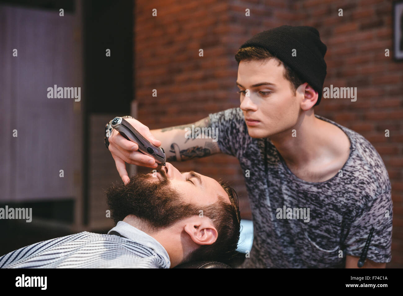 Concentrated skillful young barber trimming beard of handsome young man in barbershop Stock Photo