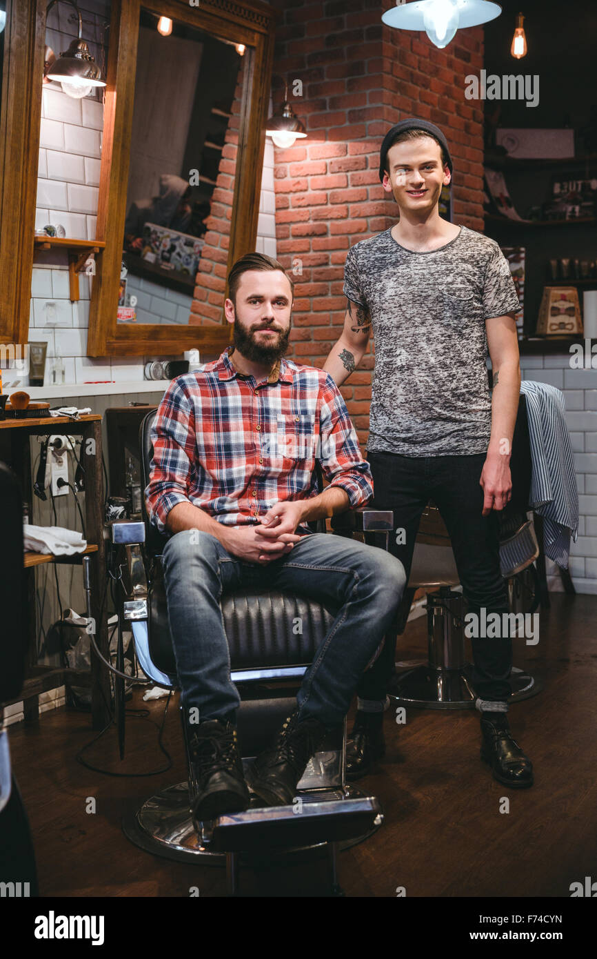 Portrait of young modern barber and his handsome content bearded client in barbershop Stock Photo