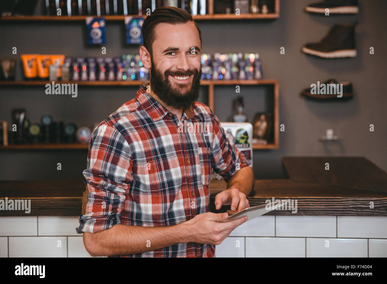 Handsome happy man with beard in plaid shirt using tablet in barbershop Stock Photo