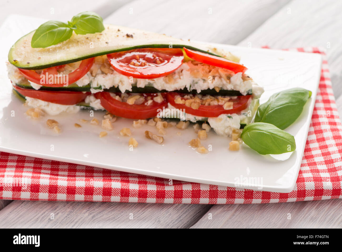 Delicious Italian appetizer of tomato, zucchini slices, nuts, basil and fresh cheese. Stock Photo