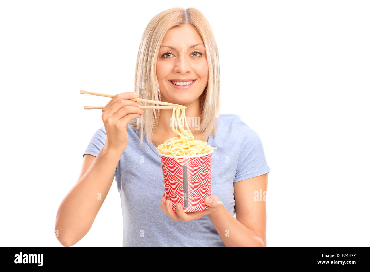 Cheerful young woman eating noodles with Chinese sticks and looking at the camera isolated on white background Stock Photo