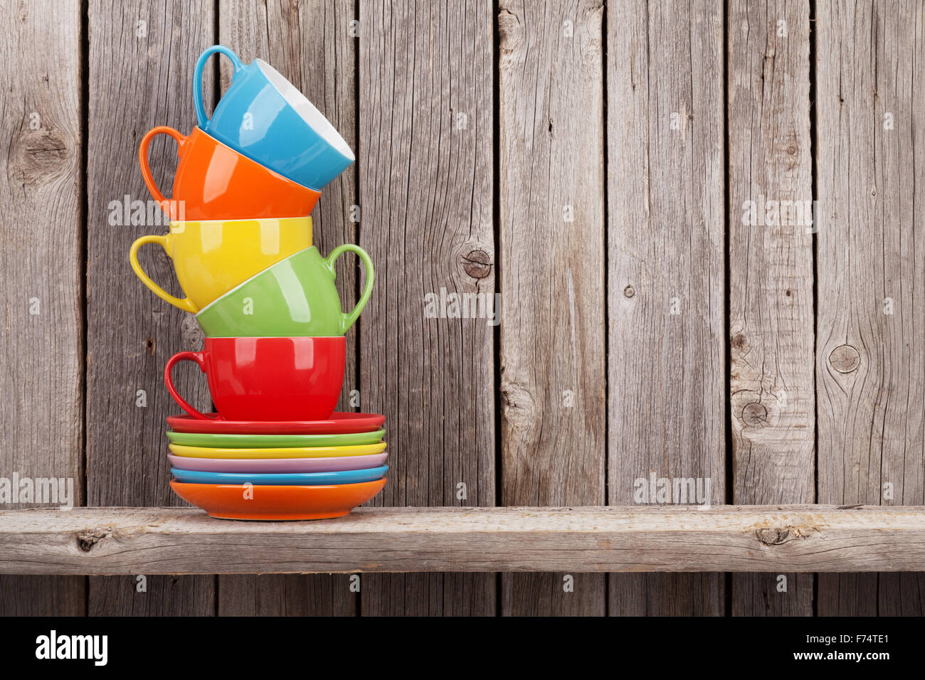Colorful coffee cups on shelf against rustic wooden wall with copy space Stock Photo