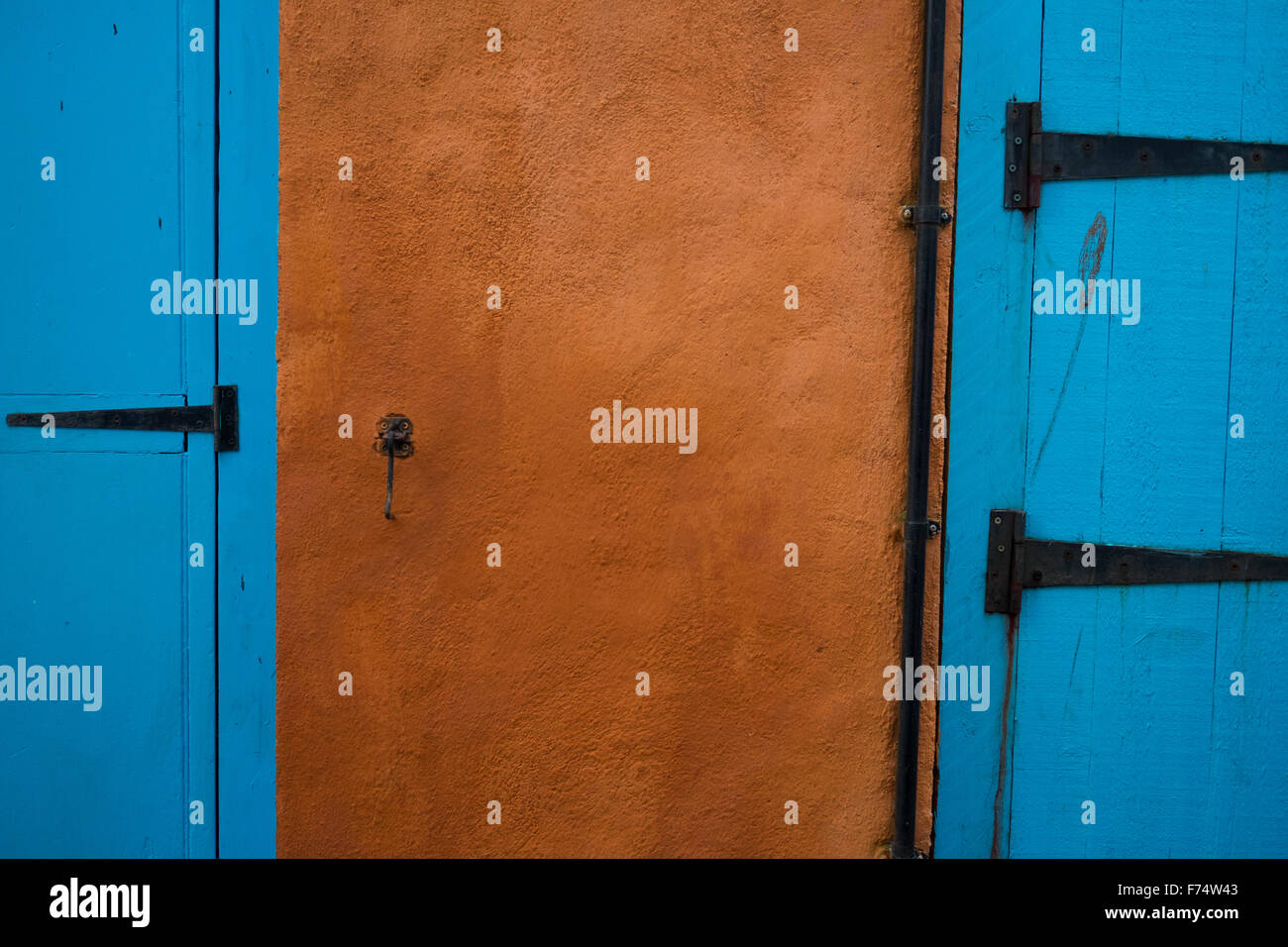 Pair of blue doors with black metal hinges against a burnt orange background - Falmouth, Cornwall. Stock Photo