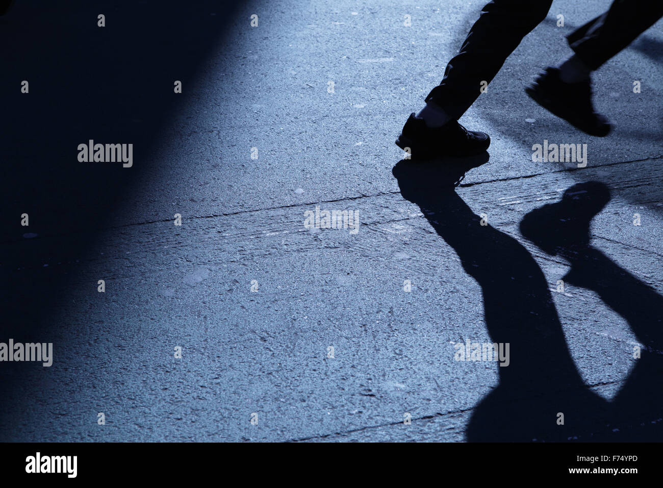 Blue night shadows and silhouette of an unrecognizable male youth legs running out of frame down a city street Stock Photo