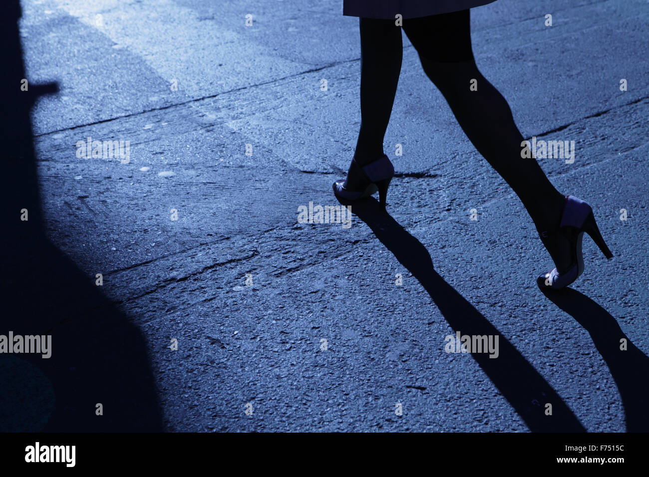 Blue night shadows and silhouette of the legs of an unrecognizable woman walking alone after dark down a city street Stock Photo