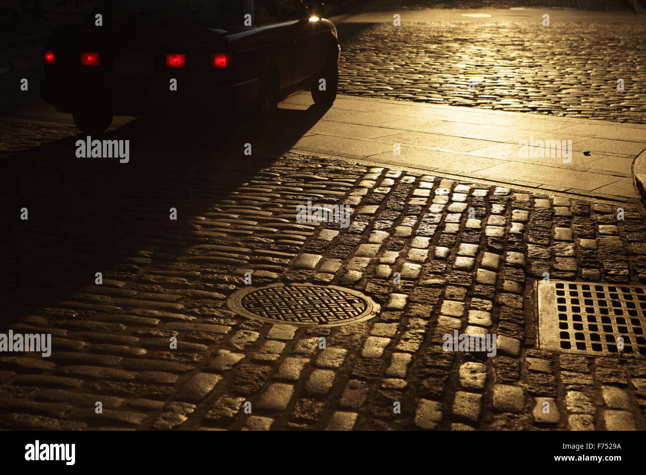 Car driving in golden sunset shadows on cobblestone street Stock Photo ...