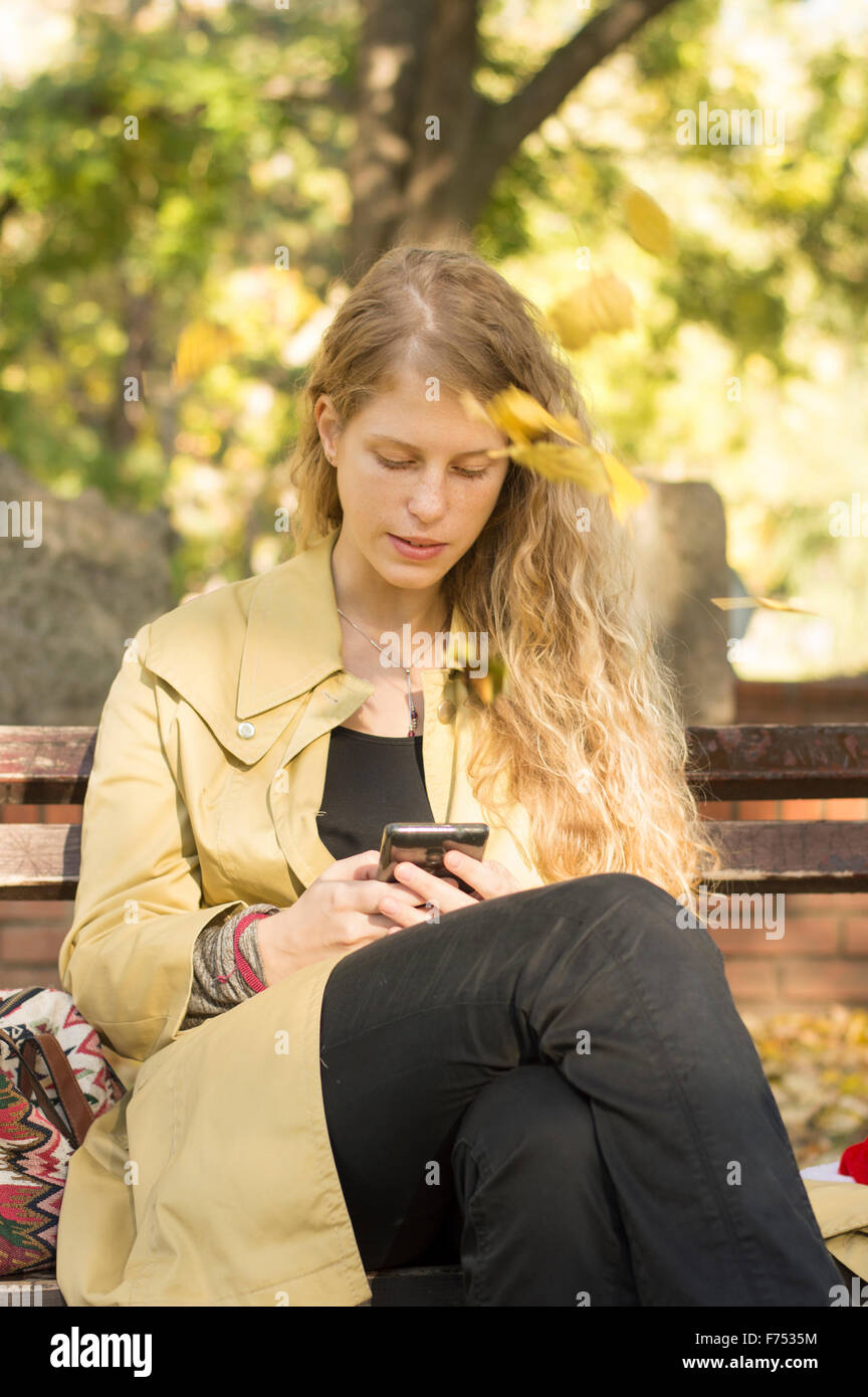 Blonde girl writing text in a park while leaves are falling Stock Photo