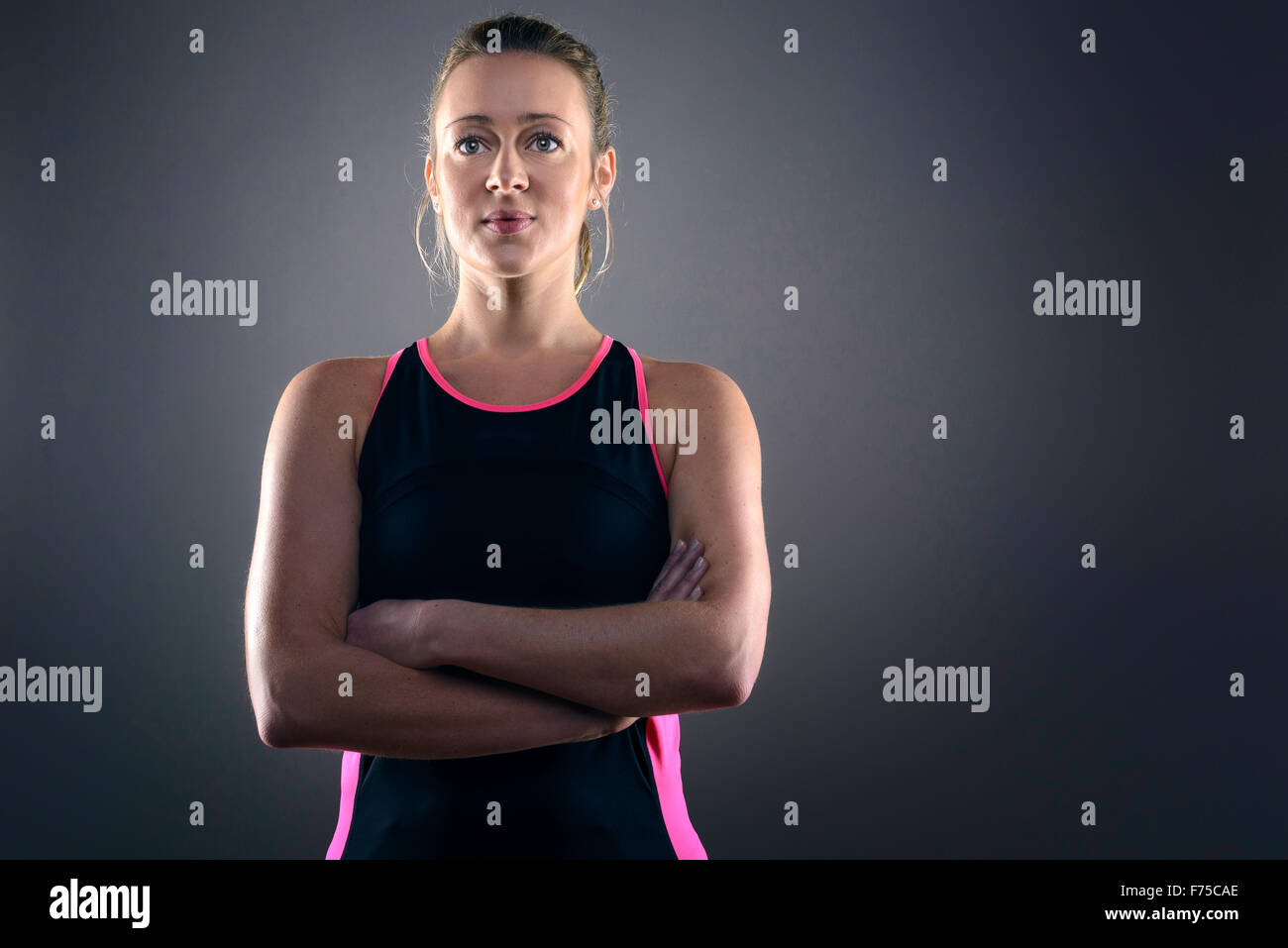 Head and Shoulders Portrait of Confident Athletic Blond Woman Wearing Pink and Black Tank Top and Standing with Hands on Hips in Stock Photo